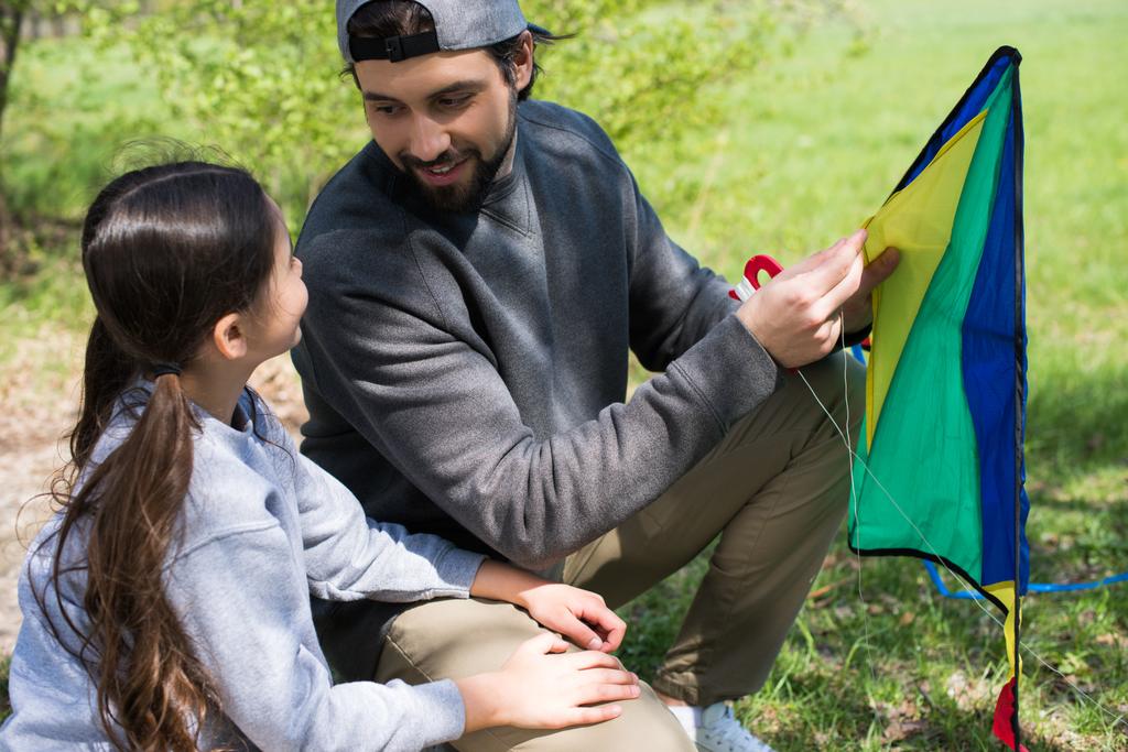vader en dochter zitten met kite op weide - Foto, afbeelding