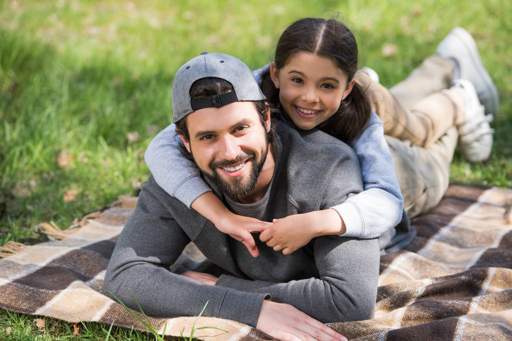 Glückliche Tochter liegt im Park auf dem Rücken ihres Vaters  - Foto, Bild
