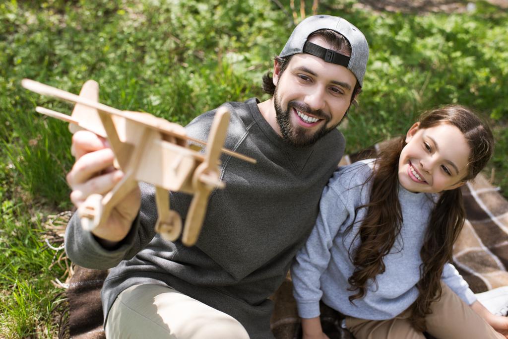 улыбающиеся отец и дочь играют с деревянным игрушечным самолетом на клетке в парке
 - Фото, изображение