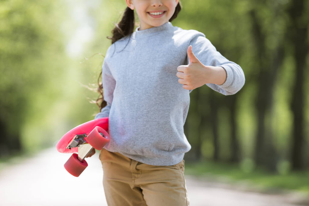 cropped image of child with penny board doing thumb up gesture - Photo, Image
