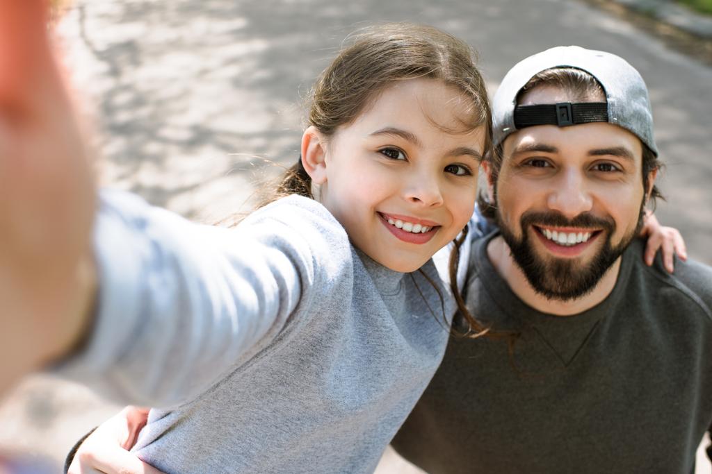 Κόρη λαμβάνοντας αυτοπορτρέτα χαμογελά πατέρα στο πάρκο - Φωτογραφία, εικόνα