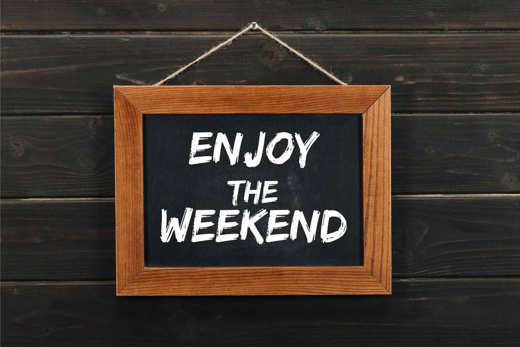 blackboard with enjoy the weekend inscription hanging on wooden wall  - Photo, Image