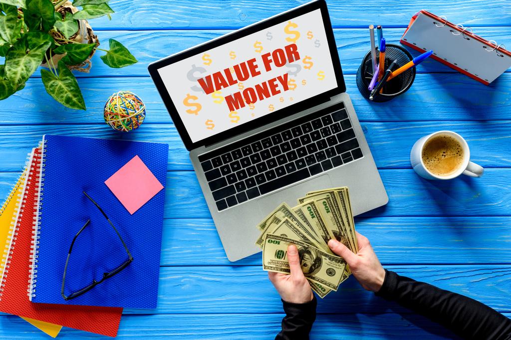Persona de negocios contando dólares por computadora portátil en mesa de madera azul con papelería, Relación calidad-precio
  - Foto, Imagen