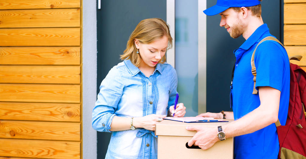 ブルーのユニフォームを着た笑顔の配達人が宅配便サービスのコンセプトを受け取るために小包ボックスを提供します。笑顔配達人で青い制服 - 写真・画像