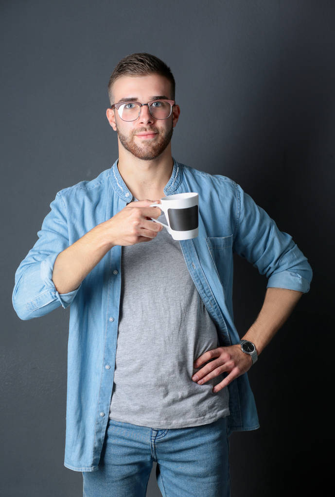 Porträt eines gutaussehenden jungen Mannes, der eine Tasse Kaffee in den Händen hält - Foto, Bild