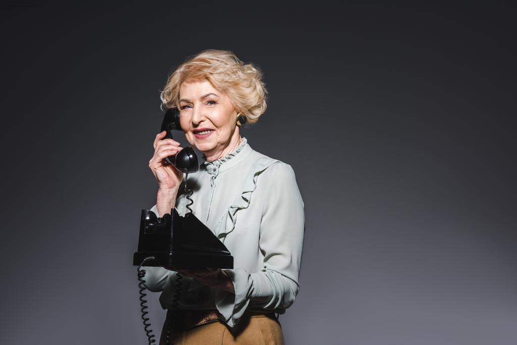 usměvavá starší žena mluví o vinobraní telefon na tmavě šedá - Fotografie, Obrázek