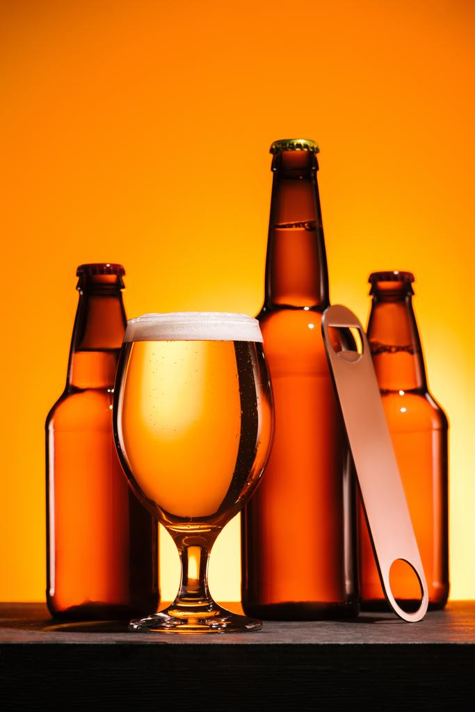Zamknij widok butelki piwa z pianki i otwieraczem do butelek na pomarańczowym tle - Zdjęcie, obraz