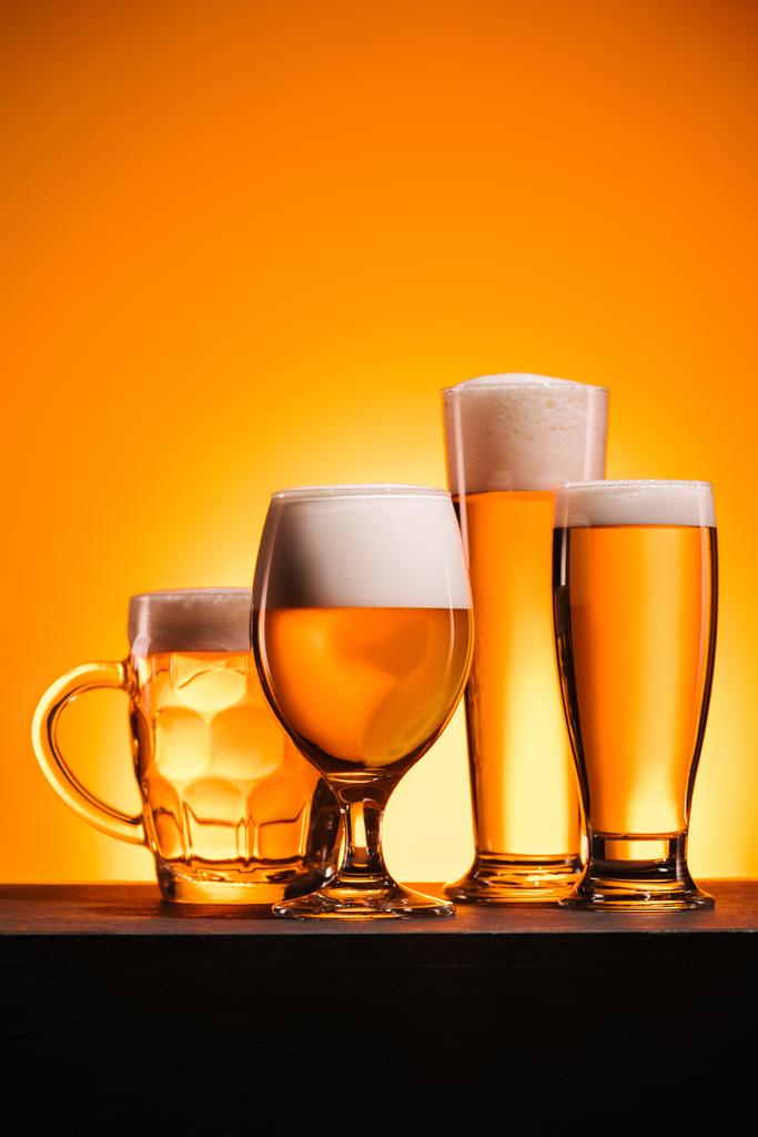 κλείνω πάνω θέα από κούπες με κρύα μπύρα με αφρό τοποθετημένα σε πορτοκαλί φόντο - Φωτογραφία, εικόνα