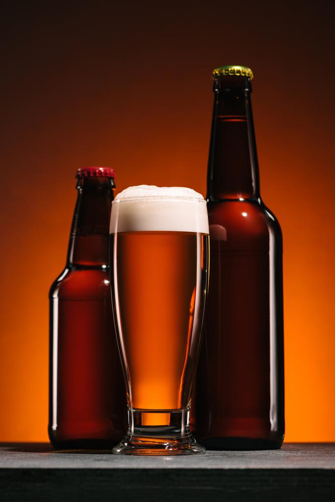 vue rapprochée des bouteilles et tasse de bière avec mousse sur fond orange
 - Photo, image