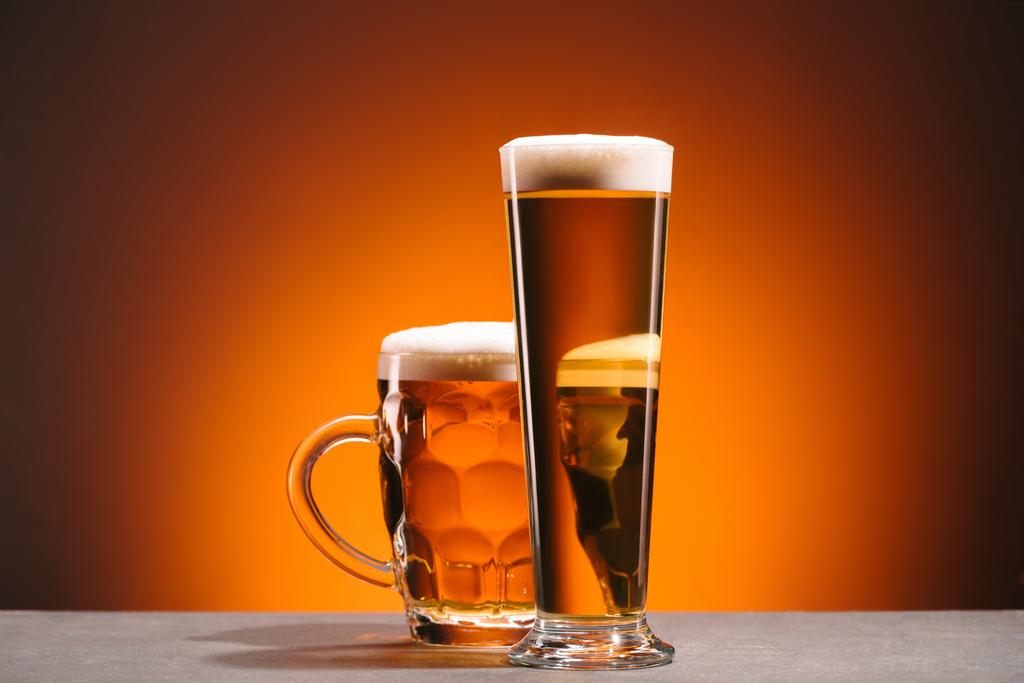 κλείνω πάνω θέα του διακανονισμού του ποτήρια μπύρας με αφρό σε πορτοκαλί φόντο - Φωτογραφία, εικόνα