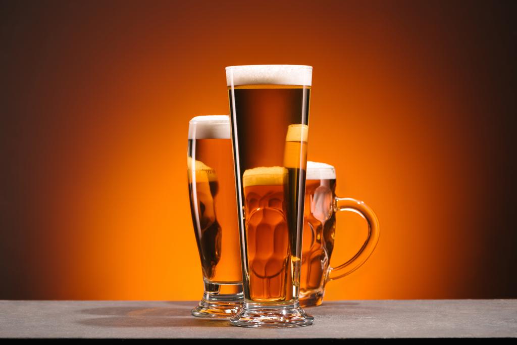 κλείνω πάνω θέα του διακανονισμού του ποτήρια μπύρας σε πορτοκαλί φόντο - Φωτογραφία, εικόνα