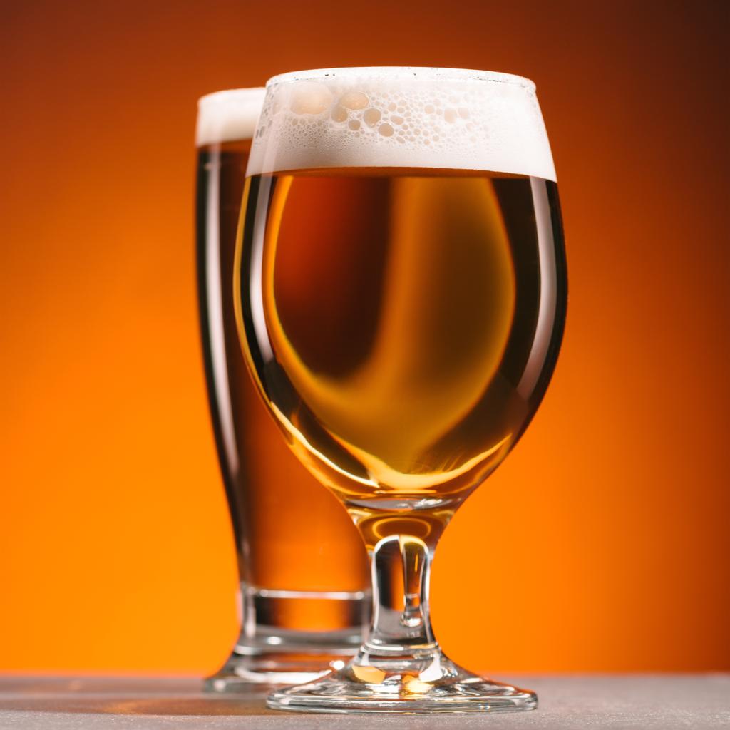 selective focus of arrangement of glasses of beer with froth on orange backdrop - Photo, Image