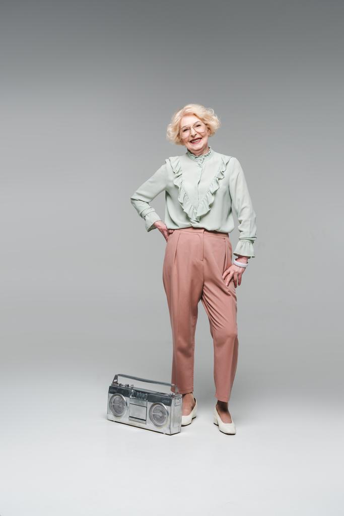 стильная пожилая женщина с винтажным бумбоксом, изолированным на сером
 - Фото, изображение