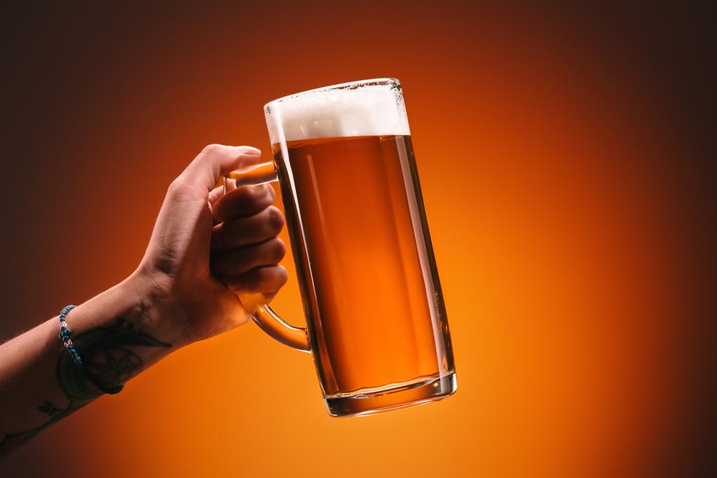 Schnappschuss einer Frau, die ein Glas kaltes Bier mit Schaum auf orangefarbenem Hintergrund hält - Foto, Bild