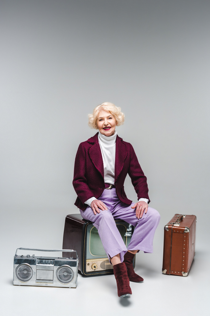 ευτυχής ανώτερος γυναίκα που κάθεται στο vintage tv στο γκρι - Φωτογραφία, εικόνα