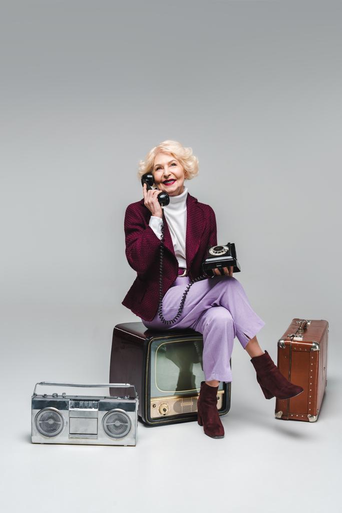 bella donna anziana parlando per telefono mentre seduto sulla tv vintage su grigio
 - Foto, immagini