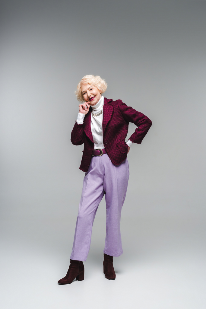 mujer mayor sonriente en ropa elegante mirando a la cámara en gris
 - Foto, Imagen