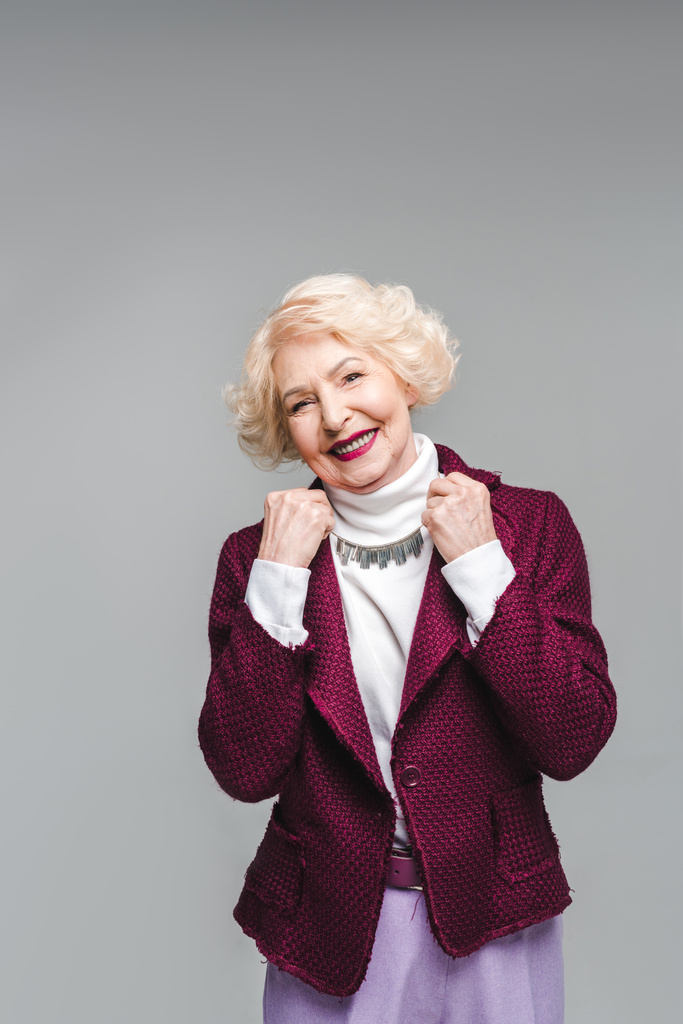 mujer mayor sonriente en chaqueta elegante y cuello alto aislado en gris
 - Foto, imagen
