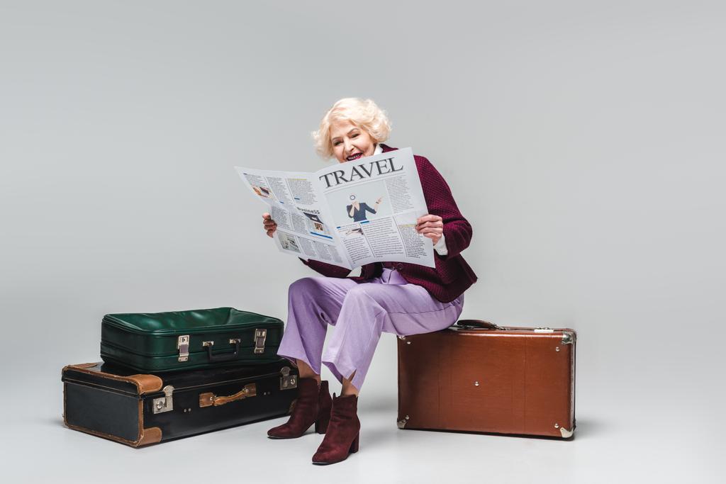ヴィンテージ スーツケースの上に座って、グレーの旅行新聞を読んで美しい年配の女性 - 写真・画像