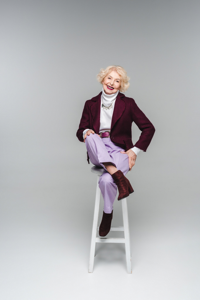 mujer mayor feliz en ropa elegante sentado en la silla en gris
 - Foto, Imagen