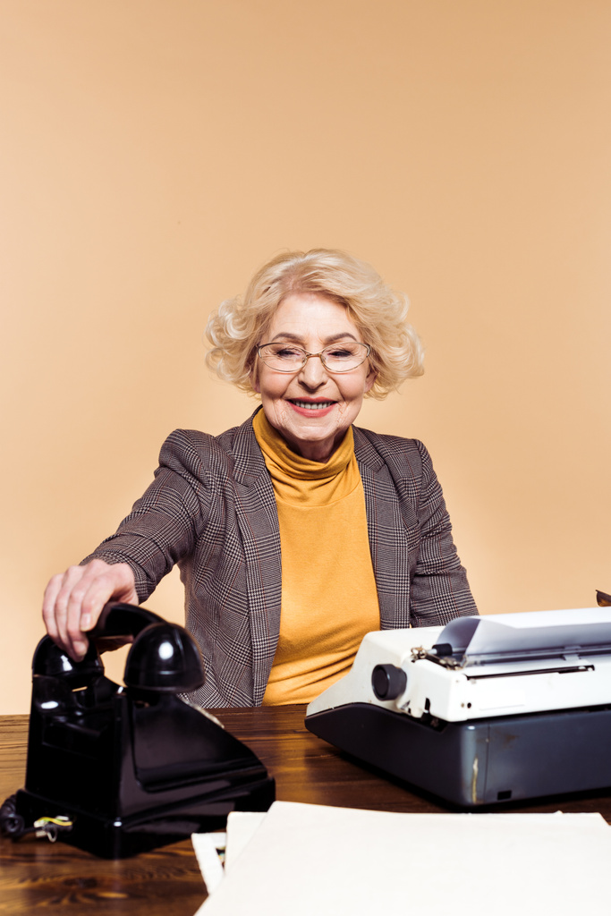 стильная пожилая женщина кладет ротационный телефон за стол с пишущей машинкой
  - Фото, изображение