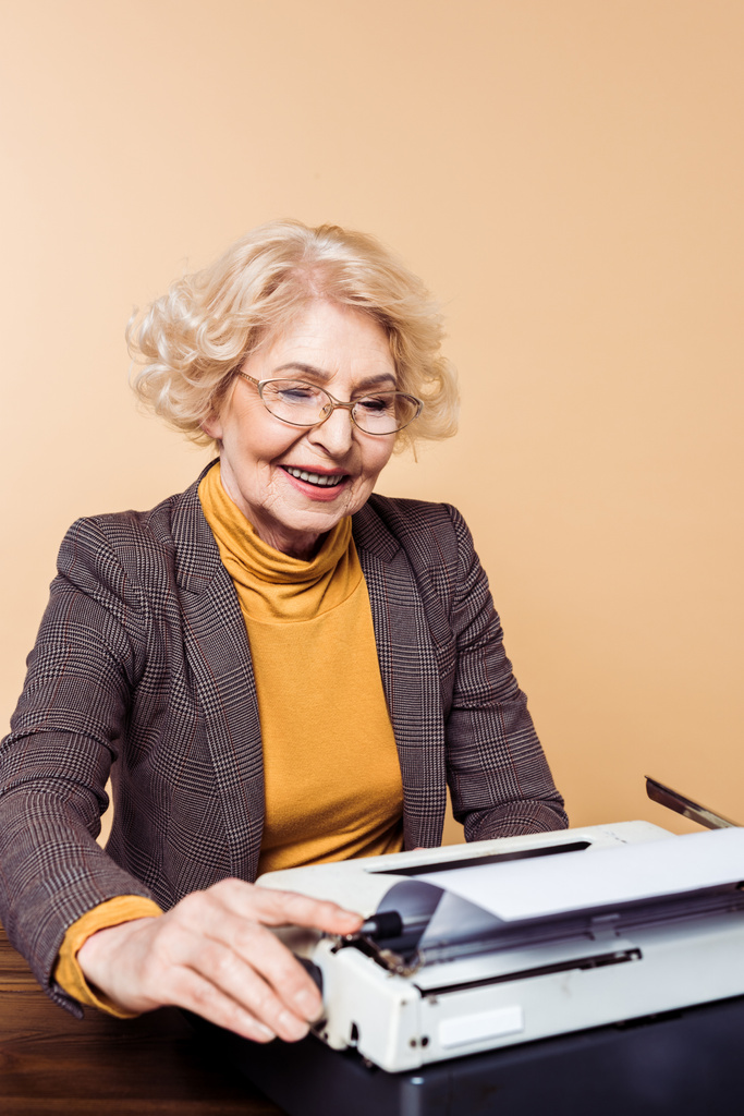 タイプライターを使って眼鏡で笑顔のスタイリッシュな年配の女性  - 写真・画像