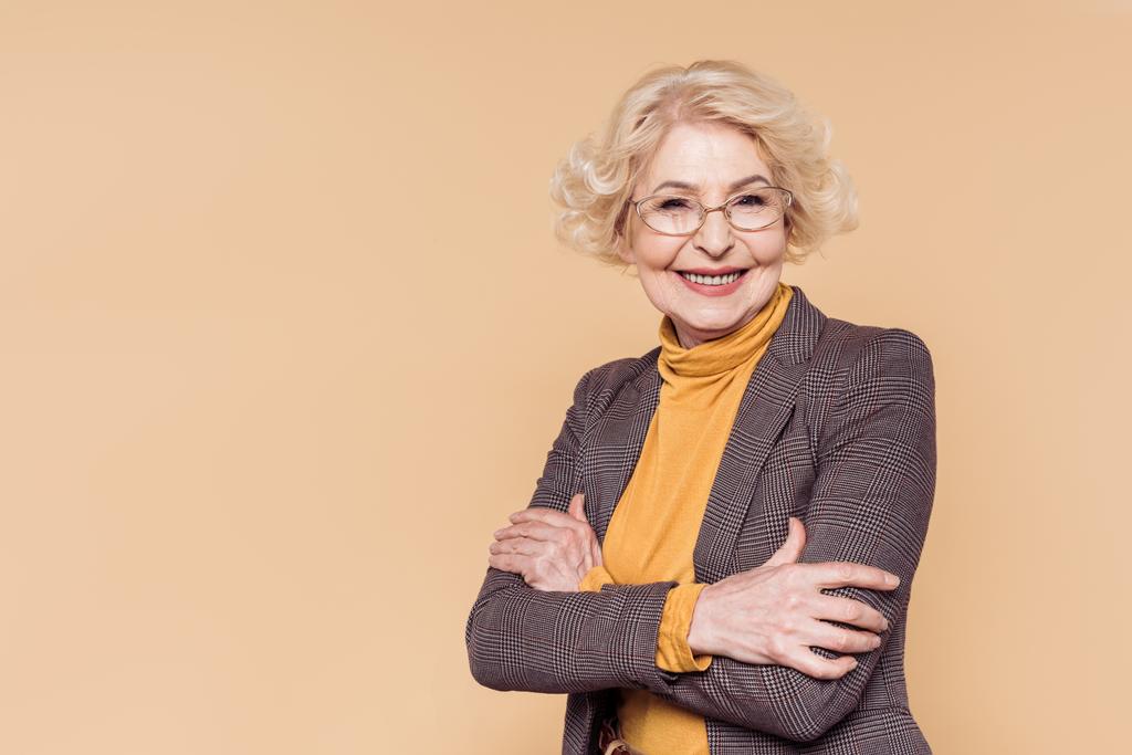 sorridente donna anziana alla moda in occhiali posa isolata su sfondo beige
  - Foto, immagini