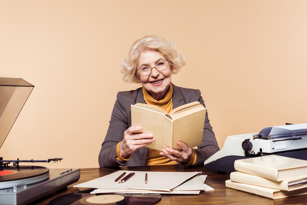 donna anziana sorridente in occhiali con libro seduta a tavola con disco in vinile, giradischi e macchina da scrivere
  - Foto, immagini
