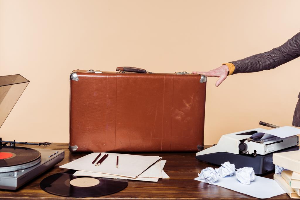 plan recadré de femme tenant la main sur une valise vintage sur table avec machine à écrire, disque vinyle et tourne-disque
  - Photo, image