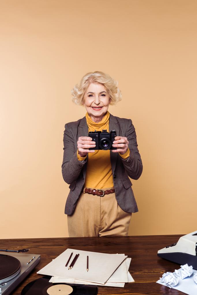 усміхнена стильна старша жінка з кінокамерою ізольована на бежевому фоні
 - Фото, зображення