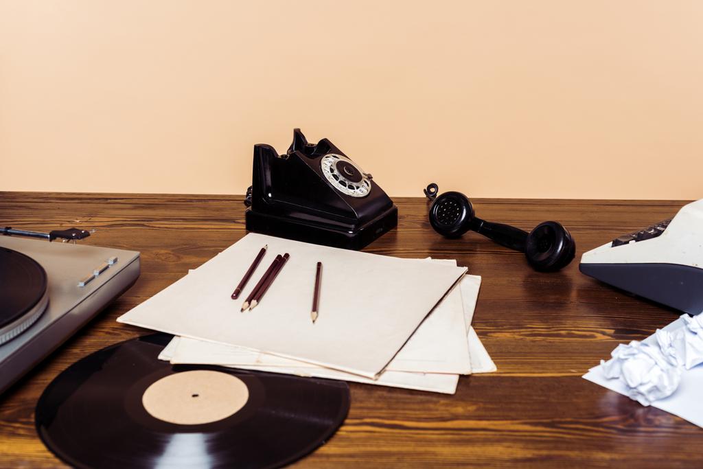 ротаційний телефон, вініловий диск, програвач запису та друкарська машинка на дерев'яному столі
  - Фото, зображення