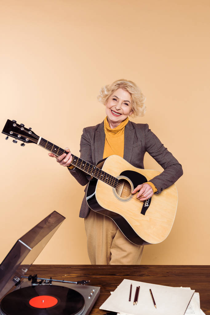 mulher sênior sorrindo tocando na guitarra acústica perto da mesa com leitor de vinil
  - Foto, Imagem