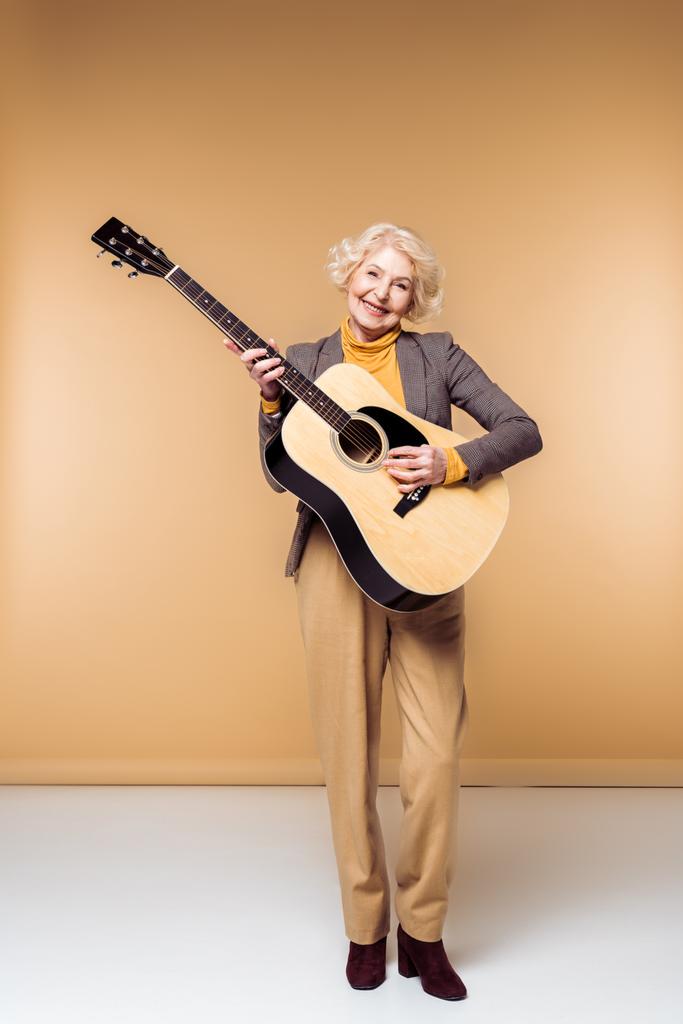 sonriente elegante senior mujer jugando en acústica guitarra
  - Foto, Imagen