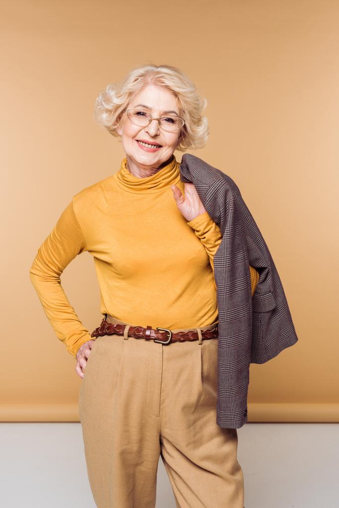 Улыбающаяся стильная пожилая женщина в очках, держащая куртку на плече
 - Фото, изображение