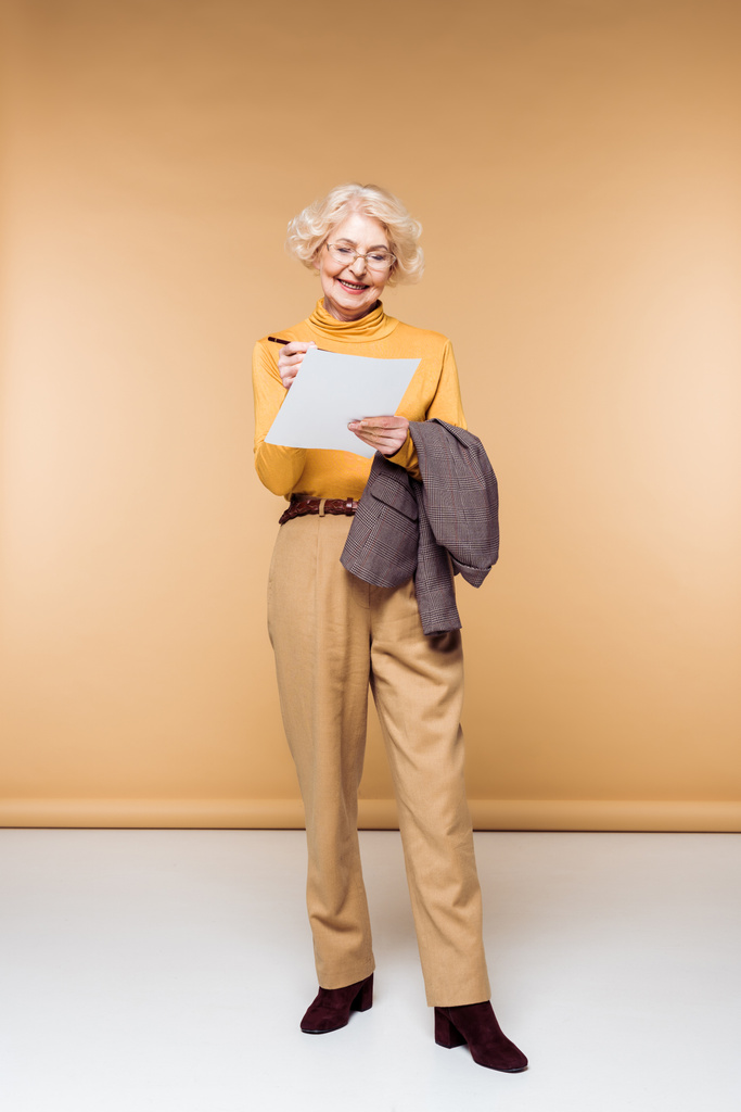 tyylikäs vanhempi nainen silmälasit tilalla takki ja kirjallisesti paperille
 - Valokuva, kuva