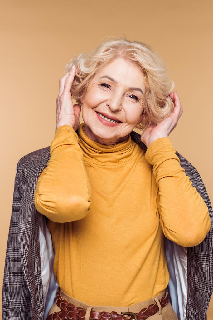  Senior kobieta z płaszcz na ramiona, dopasowywanie fryzury na białym tle na beżowym tle  - Zdjęcie, obraz