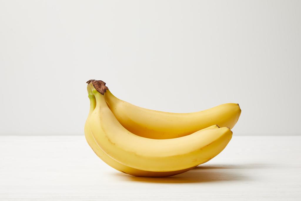 vista de cerca de plátanos maduros sobre una mesa blanca sobre fondo gris
 - Foto, imagen
