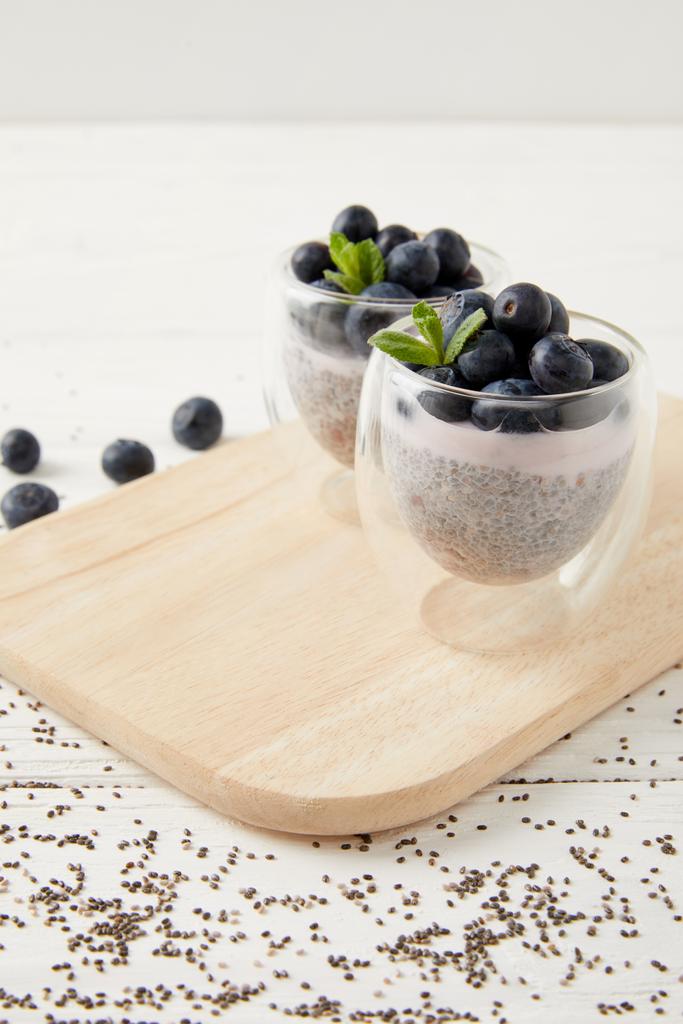 close up view of chia puddings with fresh blueberries and mint on wooden cutting board on white surface - Photo, Image
