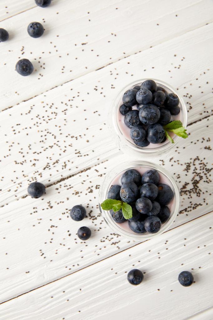 top view of arranged chia puddings with fresh blueberries and mint on white wooden surface - Photo, Image