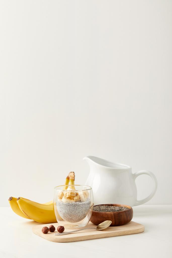 zblízka pohled chia semen pudink s kousky banánů a lískových ořechů na dřevěném prkénku s lžící - Fotografie, Obrázek