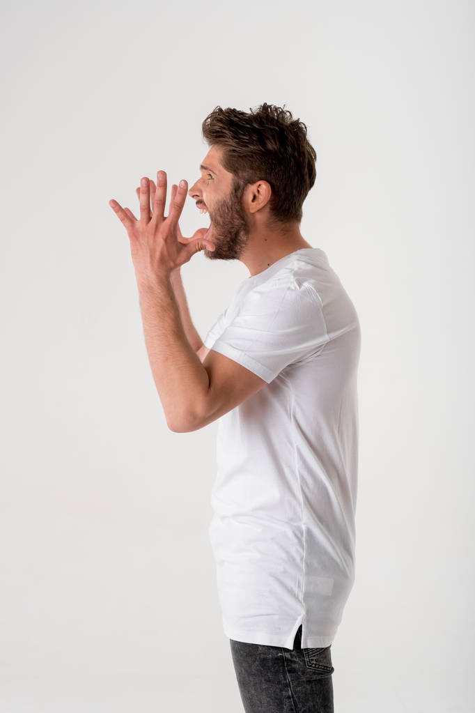 muotokuva nuoresta parrakkaasta miehestä huutamassa valkoisessa paidassa harmaalla taustalla
  - Valokuva, kuva