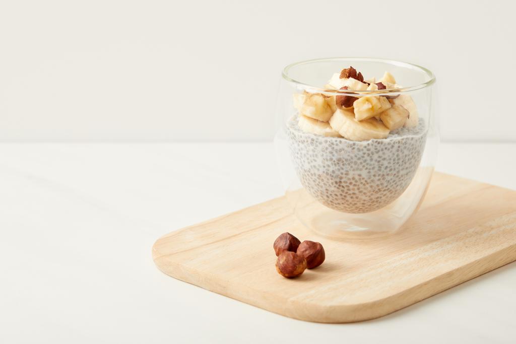 Zamknij widok smaczny chia seed pudding z kawałkami banana i orzechy laskowe na drewnianą deską do krojenia na stole - Zdjęcie, obraz