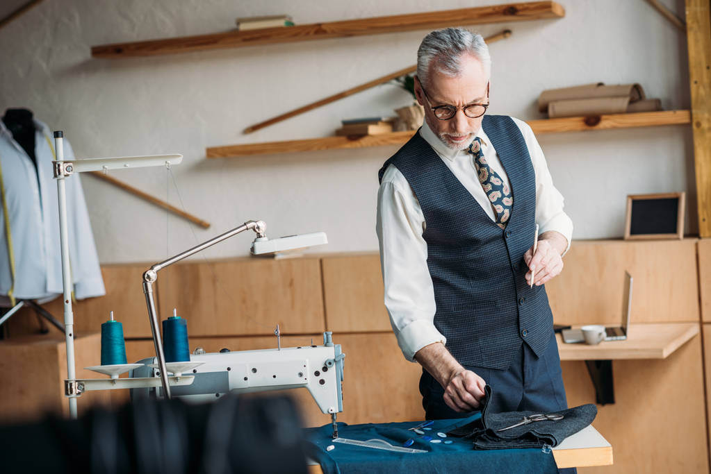 senior tailor examining cloth at sewing workshop - Photo, Image