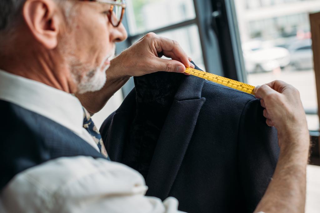 Zijaanzicht van senior kleermaker jas met meetlint op naaien workshop meten - Foto, afbeelding