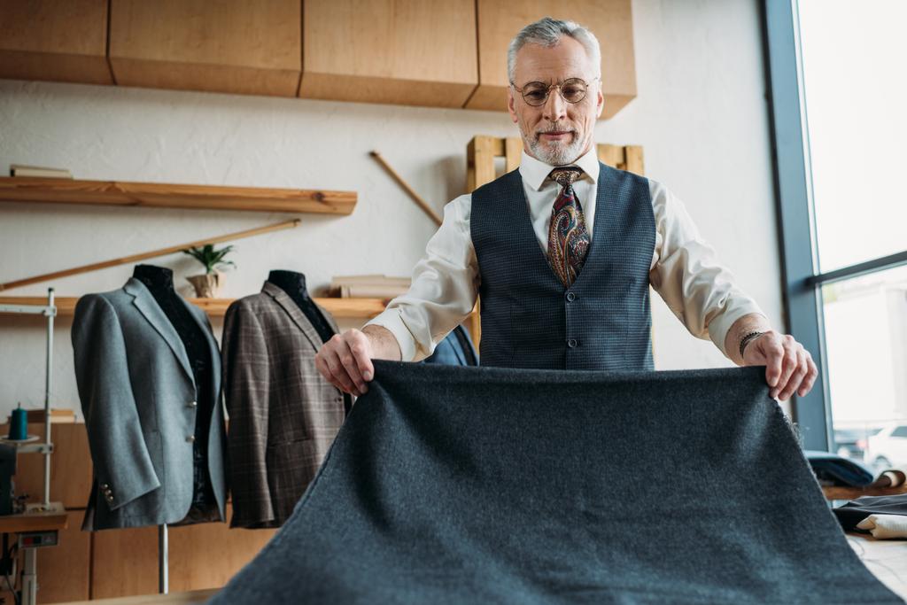serious mature tailor with grey cloth at sewing workshop - Photo, Image