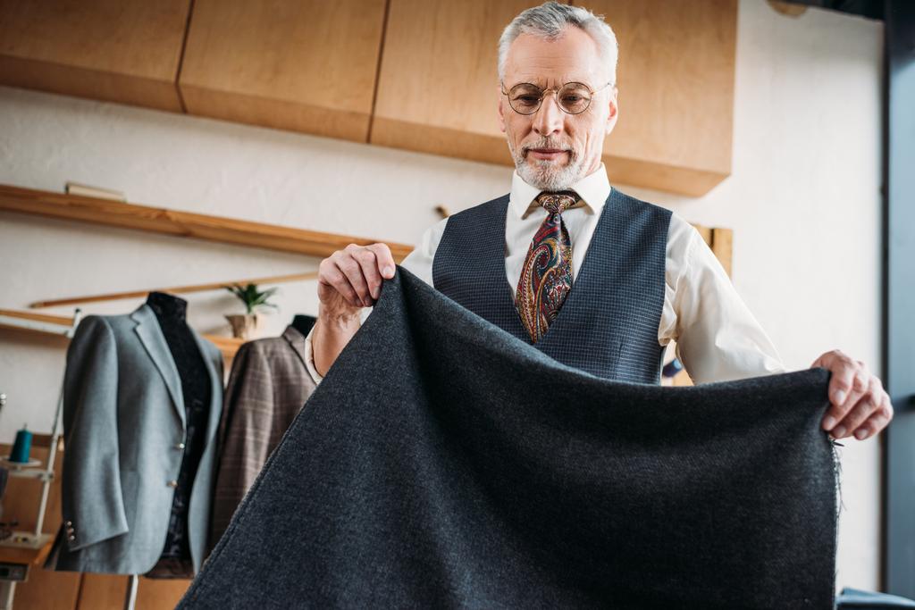 knappe volwassen kleermaker met grijze doek op naaien workshop - Foto, afbeelding