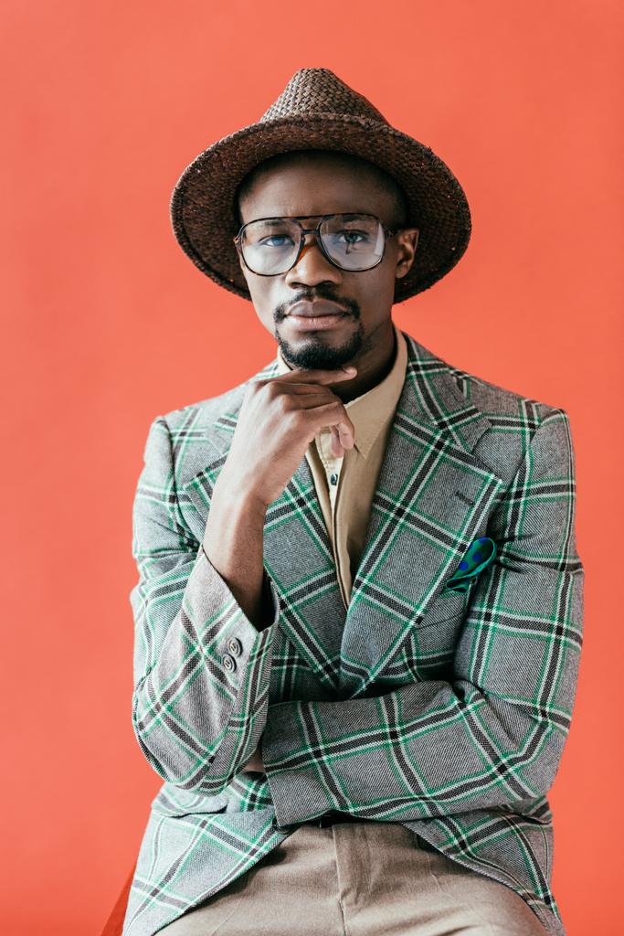 Αφρικανική αμερικανική άνθρωπος σε μοντέρνα γυαλιά και καπέλο ποζάρουν για vintage μόδα σουτ, απομονώνονται σε κόκκινο - Φωτογραφία, εικόνα