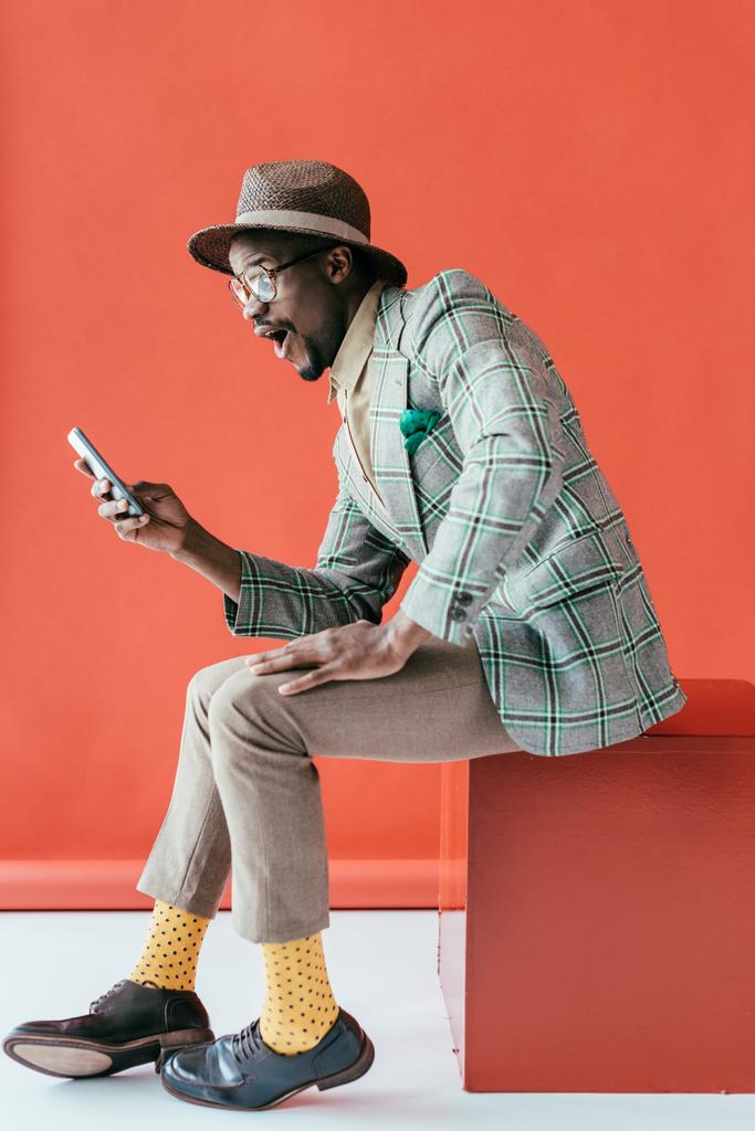 όμορφος ενθουσιασμένος αφρικανική αμερικανική άνθρωπος που χρησιμοποιούν smartphone, στο κόκκινο  - Φωτογραφία, εικόνα