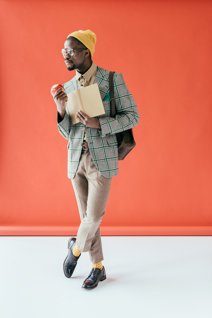 uomo afroamericano alla moda in posa con libro e mela, su rosso
 - Foto, immagini