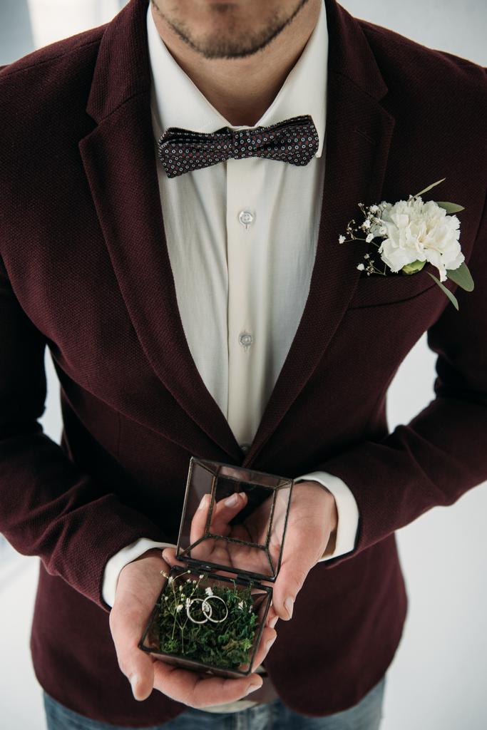 vista parcial del novio en traje con ojal y anillos de boda en caja en las manos
 - Foto, imagen
